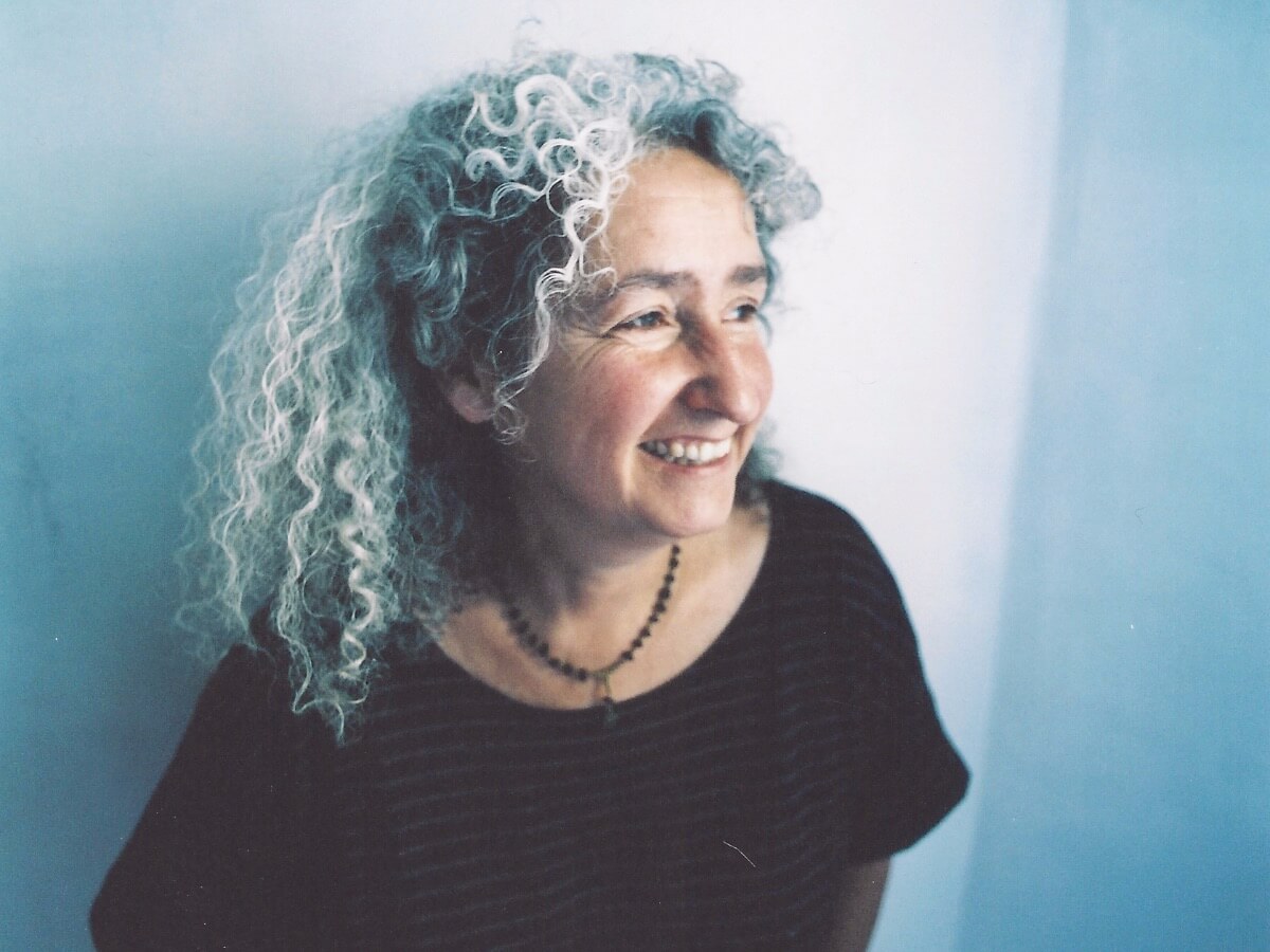 A photo of Nora Guthrie looking to the side with a blue and white wall behind her.