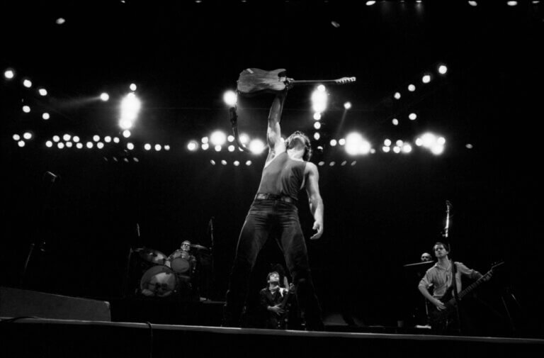 Bruce Springsteen on stage raising his guitar, black-and-white concert photo