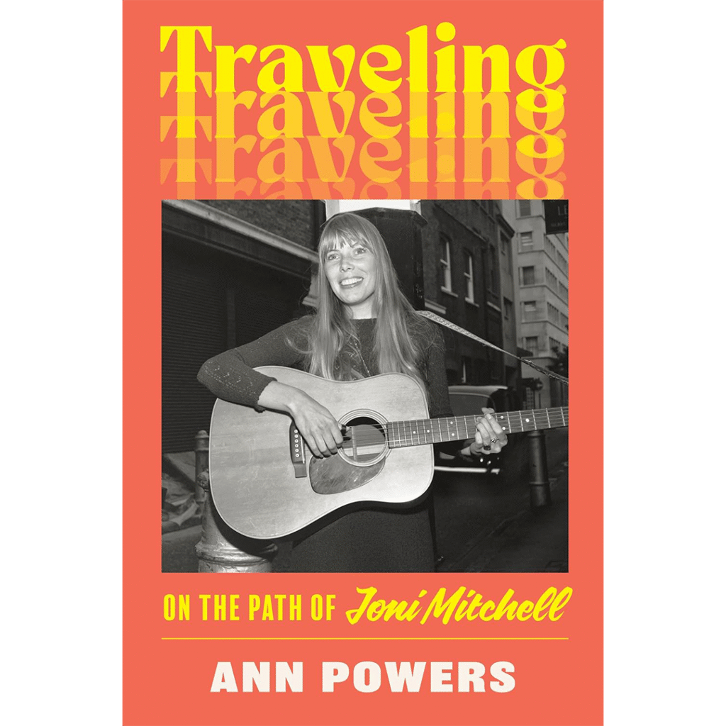 Cover of "Traveling On the Path of Joni Mitchell" by Ann Powers. Features a black and white photo of a smiling woman playing guitar on a city street. Bold yellow and white text on an orange background conveys a nostalgic tone.