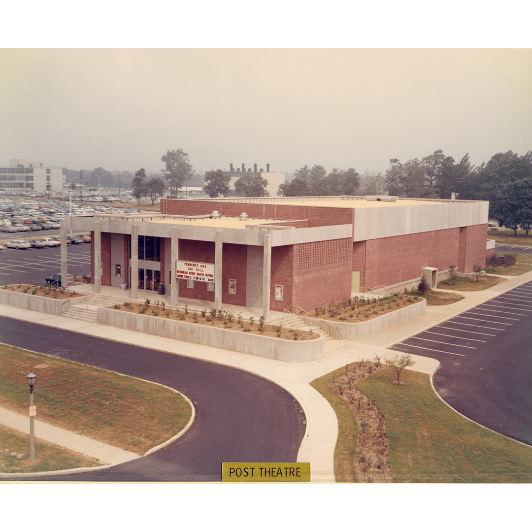 Aerial view of a large brick building labeled "Post Theatre" with marquee, surrounded by empty parking spaces, trees, and a distant parking lot.