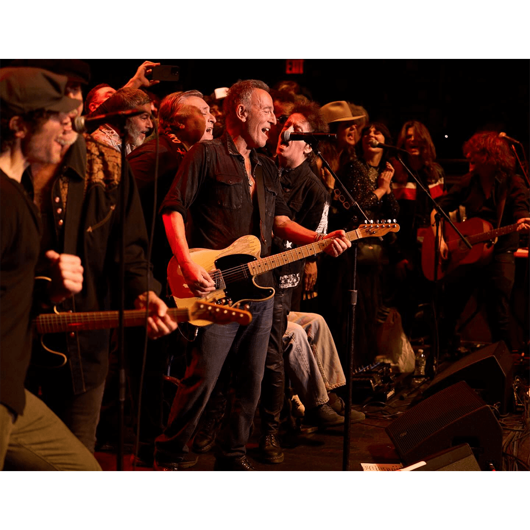 A joyful group of musicians on stage, led by a guitarist in a black shirt, passionately performing. The scene is lively and filled with energy and camaraderie.