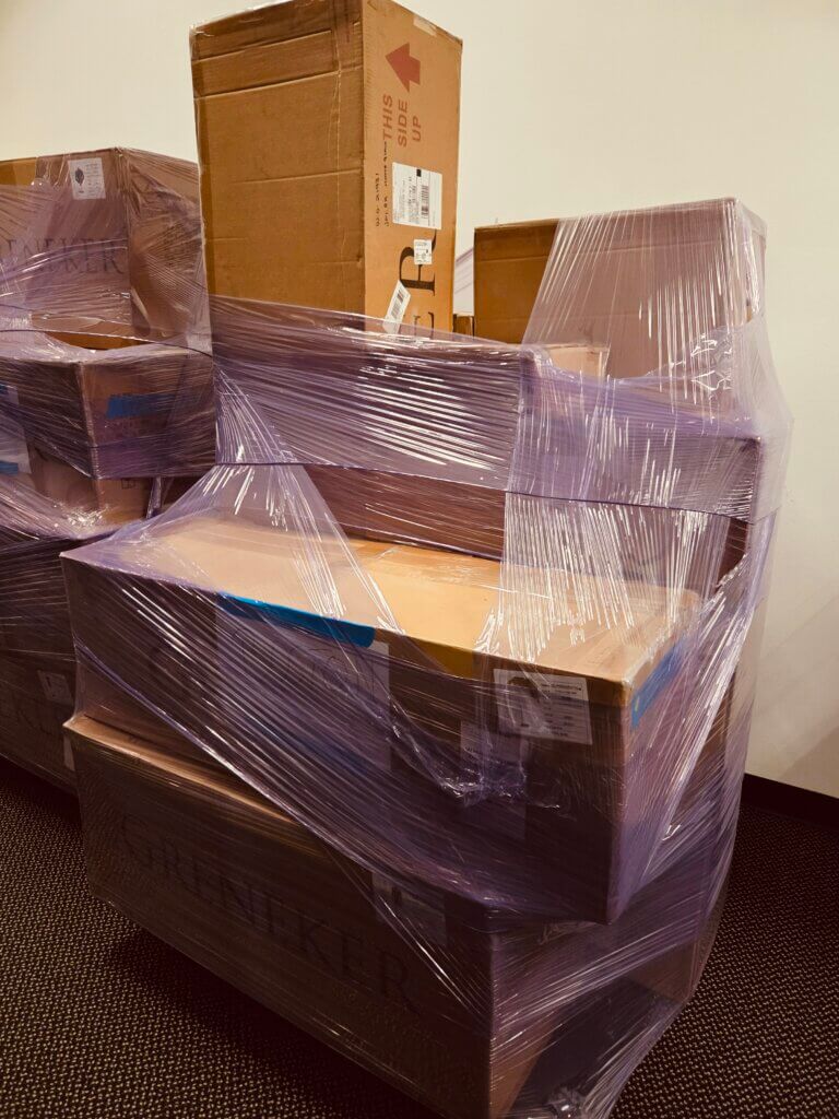 Several large cardboard boxes wrapped tightly in clear plastic are stacked against a plain wall, suggesting a recent delivery or move.