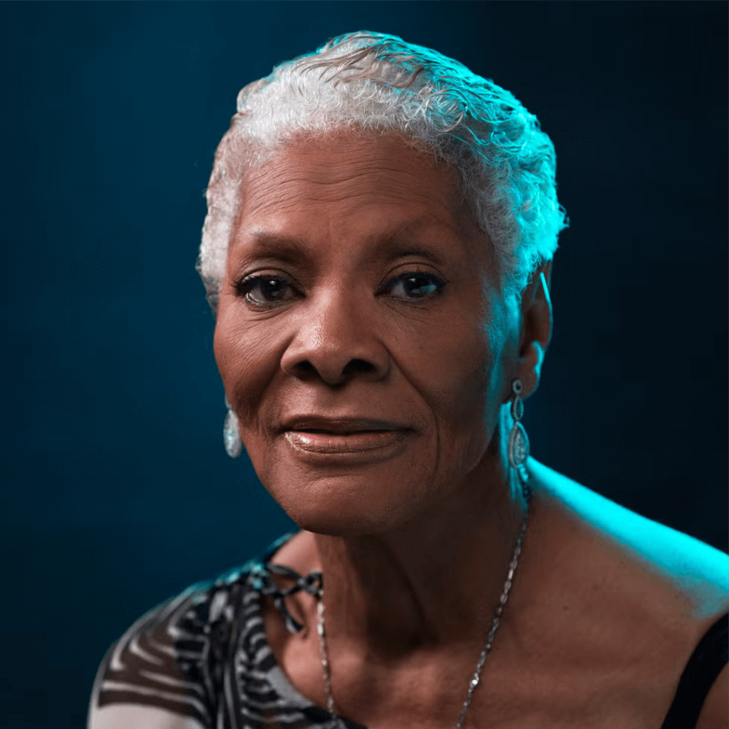 Elderly woman with short silver hair and dangling earrings, gazing calmly. The background is a soft blue, giving a serene, dignified tone.