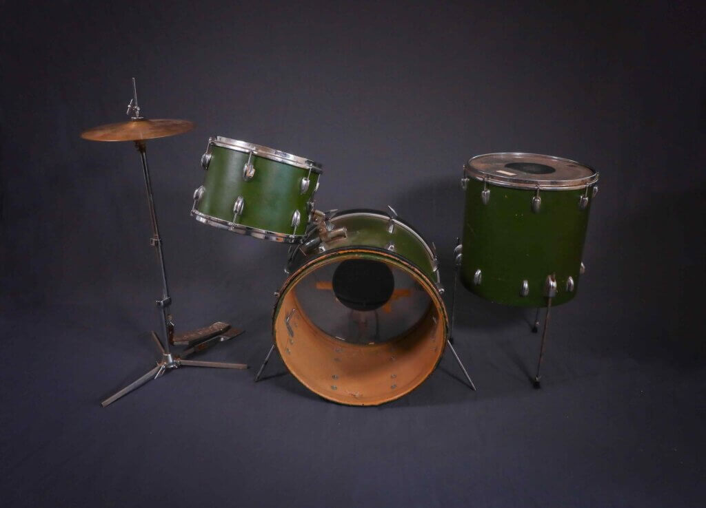 A vintage drum set with green shells on a dark background, featuring a bass drum, floor tom, mounted tom, and a single cymbal on a stand.