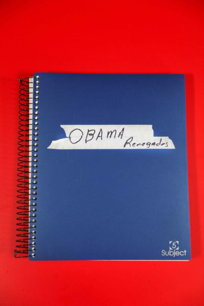 A blue spiral notebook labeled "Obama Renegades" with handwritten text on white tape, set against a vibrant red background.