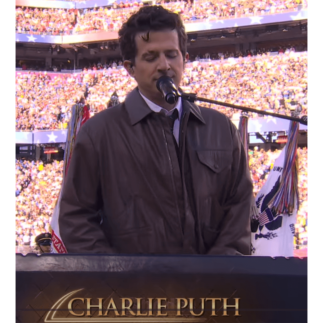 Man in a brown jacket sings into a microphone at a stadium. The background shows a large crowd, and the mood is solemn and focused. Text at the bottom reads "Charlie Puth."