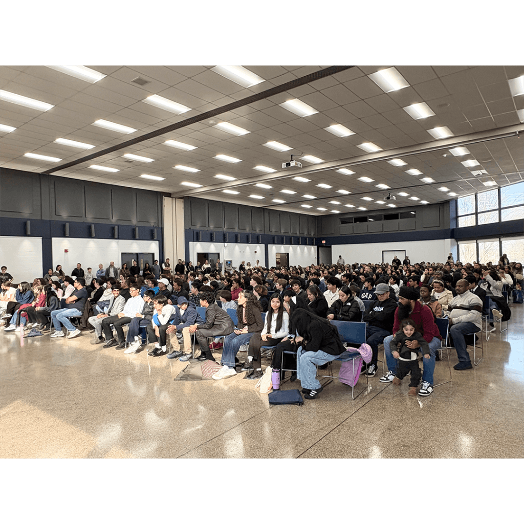 A large gathering of people seated in rows in a spacious, well-lit auditorium with high ceilings, indicating an event or ceremony. The atmosphere is attentive.