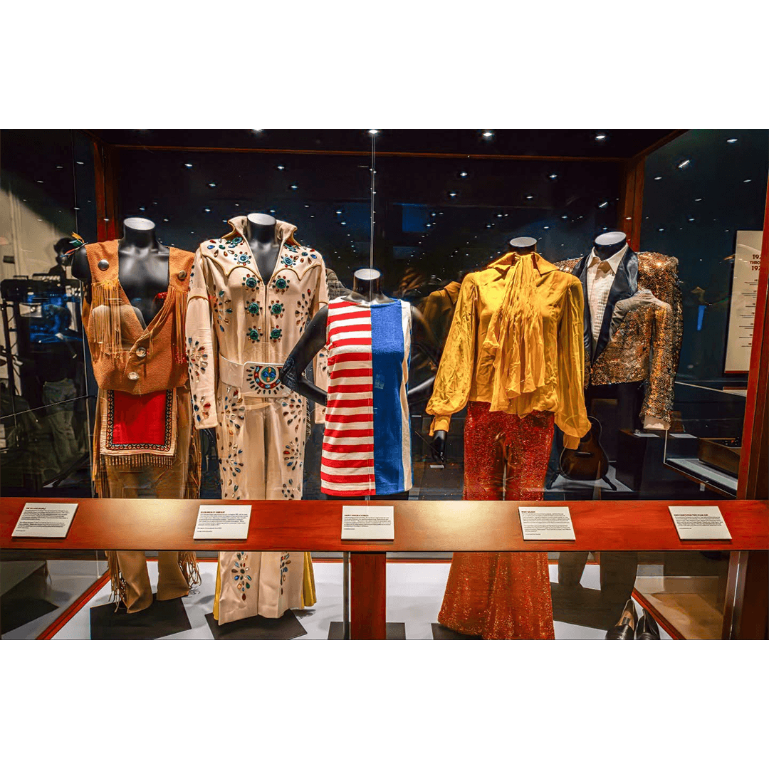 A display of five vintage outfits on mannequins in a museum exhibit. Each ensemble is unique, featuring vibrant colors, patterns, and textures.
