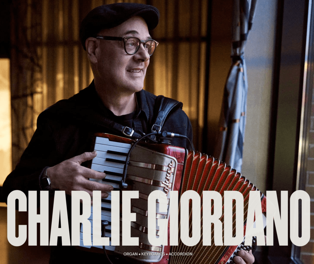 Man joyfully plays an accordion near a window, wearing glasses and a cap. Warm lighting and large text reading "Charlie Giordano" convey a musical theme.
