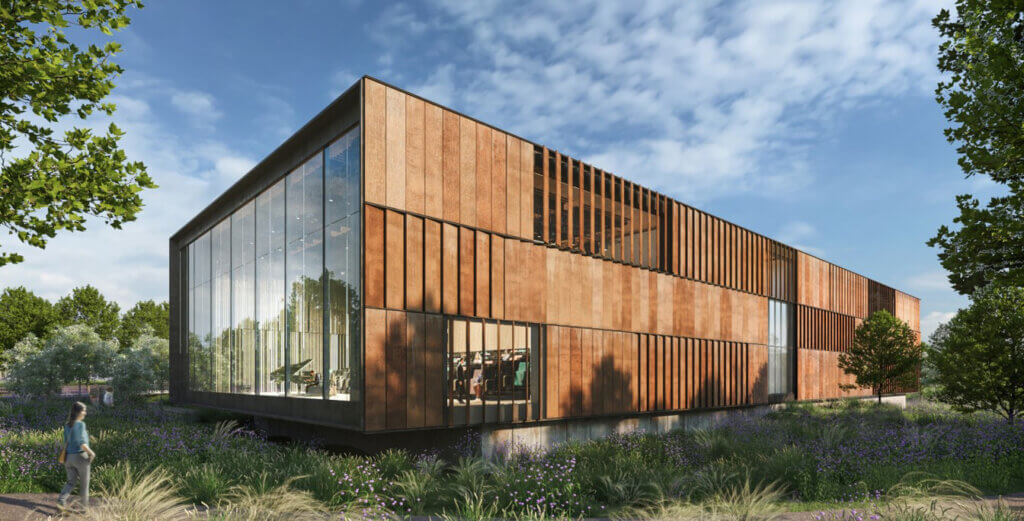 Modern building with rust-colored panels and large glass windows, surrounded by lush greenery and trees under a clear blue sky. Conveying tranquility.