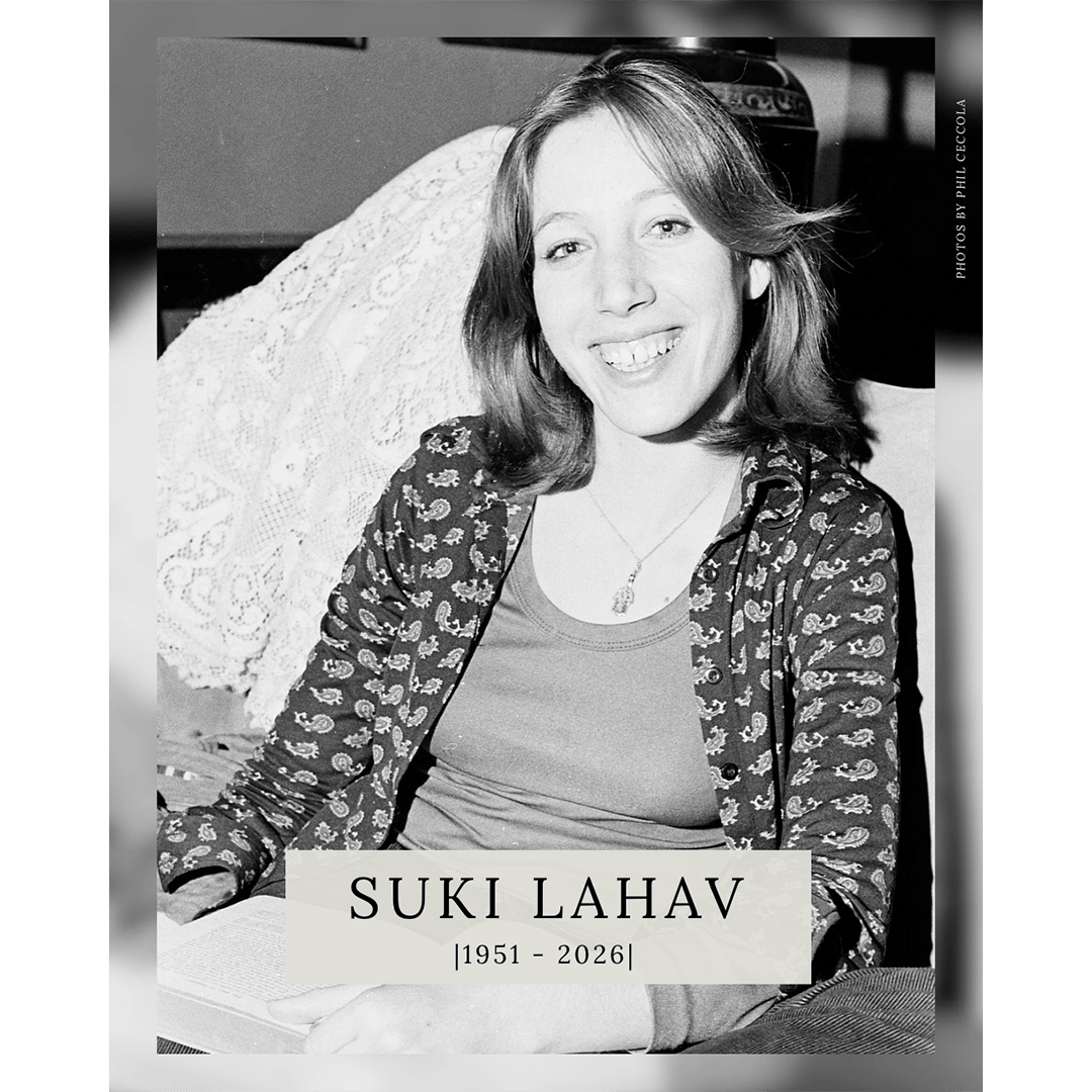 Black and white photo of a smiling woman with shoulder-length hair, wearing a patterned shirt. She is sitting indoors, and text below says "Suki Lahav, 1951-2026."