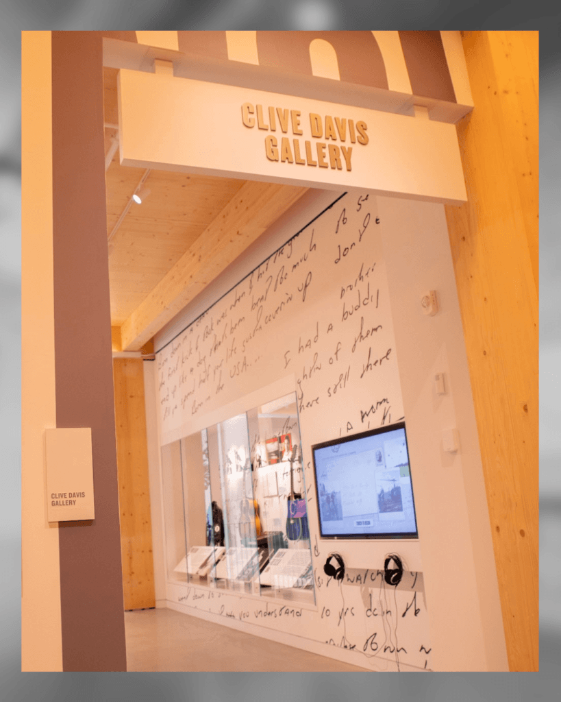 The entrance to the Clive Davis Gallery, featuring a large sign above the doorway and walls decorated with handwritten lyrics, a digital display screen, and headphones for an interactive exhibit.