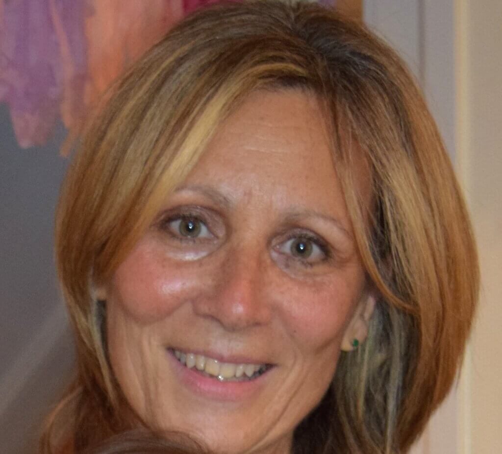 A portrait of a woman with highlighted shoulder-length hair and light-colored eyes, smiling warmly at the camera.