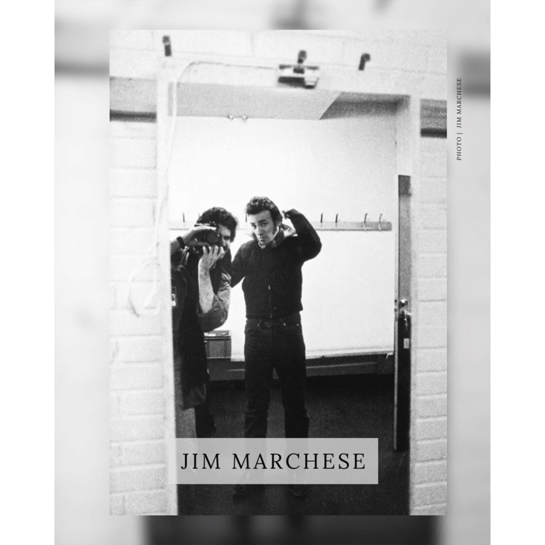 Jim Marchese's black-and-white photo of Bruce Springsteen adjusting his collar in a mirror, with Marchese reflected behind his camera.