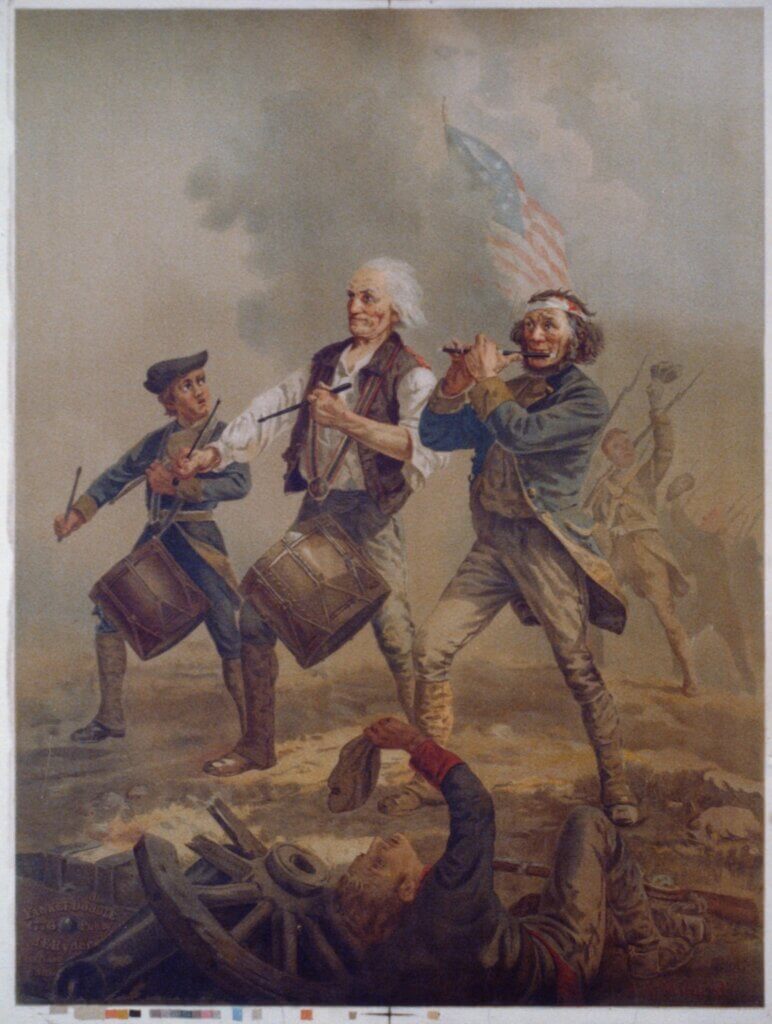 A reproduction of Archibald Willard's famous painting 'The Spirit of '76.' The scene depicts three Revolutionary War soldiers marching forward: an older man playing a drum in the center, a younger boy playing a drum to his left, and a middle-aged man playing a fife to his right. A wounded soldier lies on the ground in the foreground, while a blurred American flag and other troops are visible in the background against a smoky, battlefield sky.
