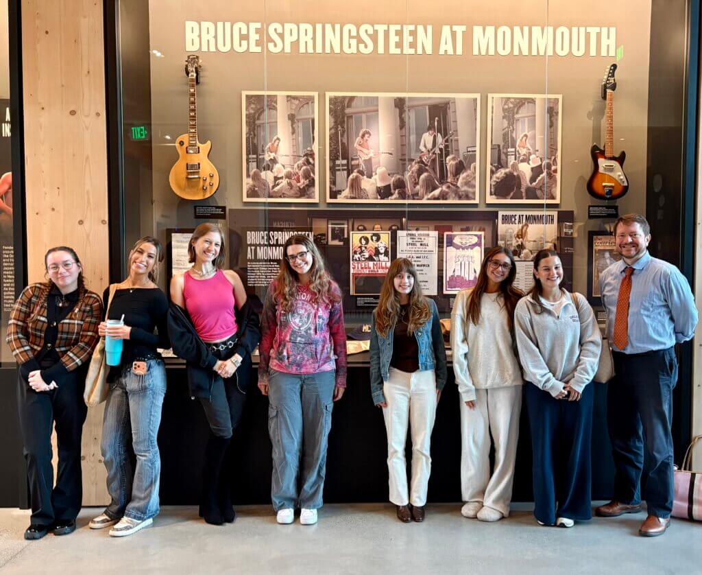 Eight people posing by the Bruce Springsteen at Monmouth display case