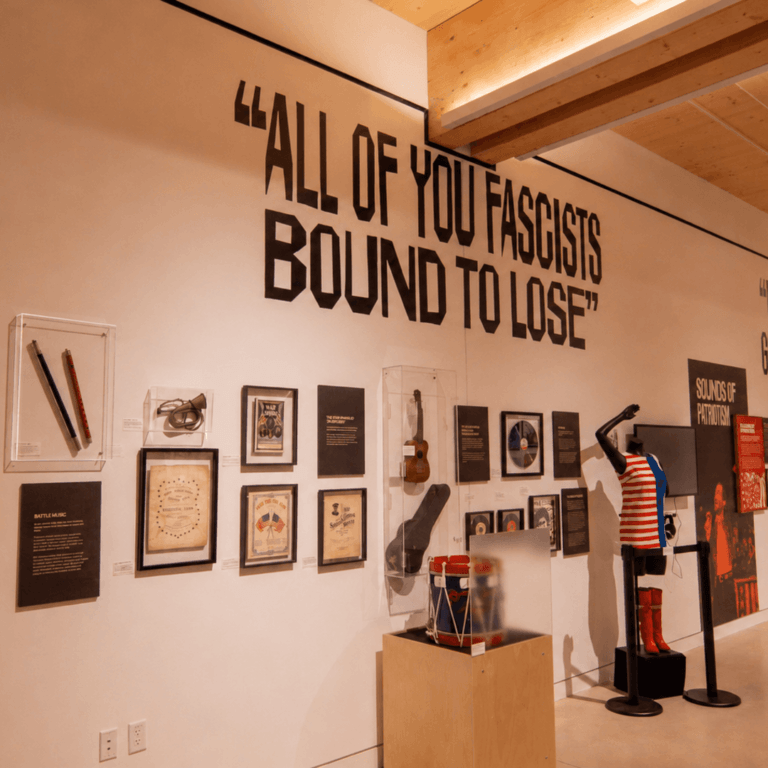 Chimes of Freedom exhibition gallery with the slogan "All of You Fascists Bound to Lose" above framed artifacts