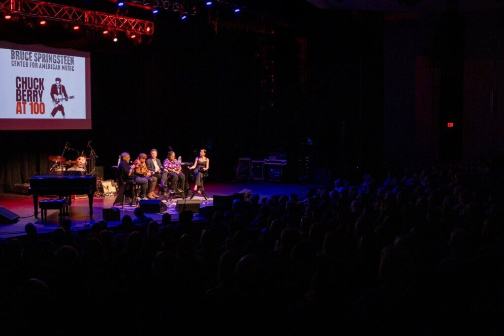 The Complicated Legacy of Chuck Berry panel on stage at Chuck Berry at 100: five panelists seated before an audience beside a Chuck Berry at 100 screen