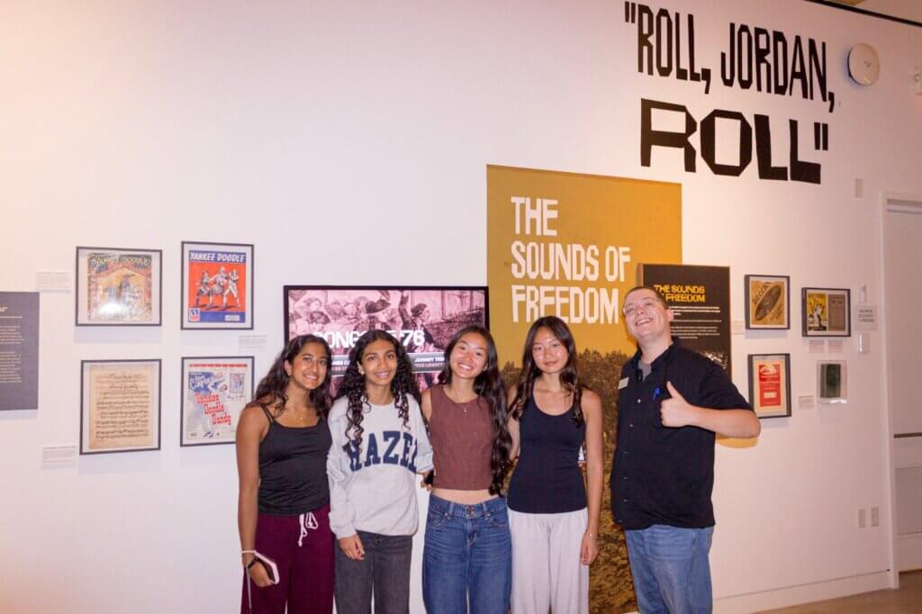 Four students and a Center staff member in the Chimes of Freedom gallery beside The Sounds of Freedom panel
